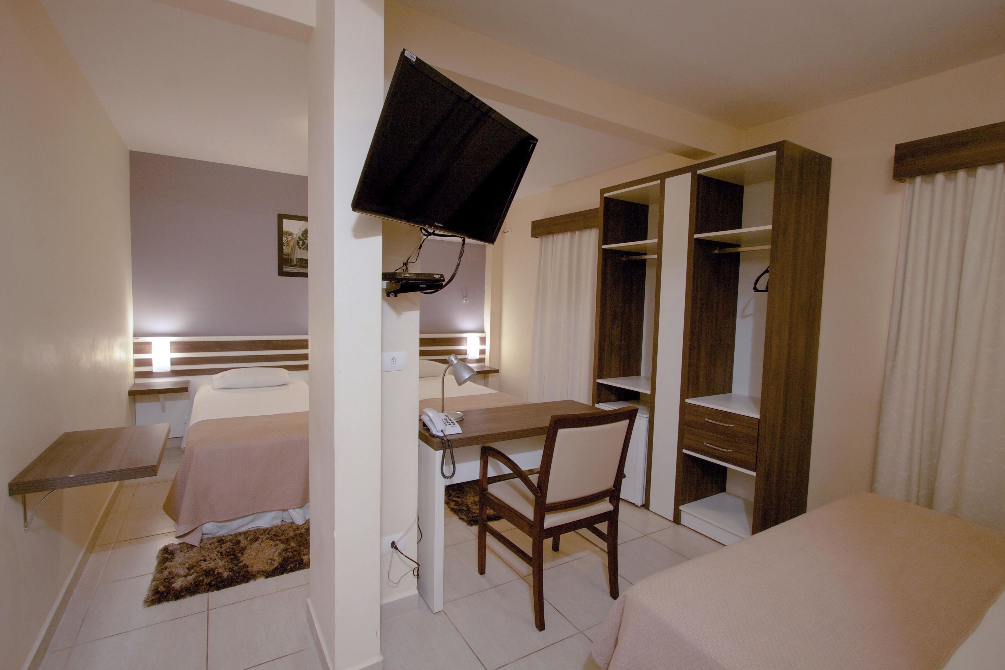 Una habitación de hotel con cama, escritorio, silla, televisor, armario y una pequeña mesa.