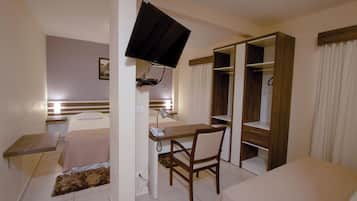 Una habitación de hotel con cama, escritorio, silla, televisor, armario y una pequeña mesa.