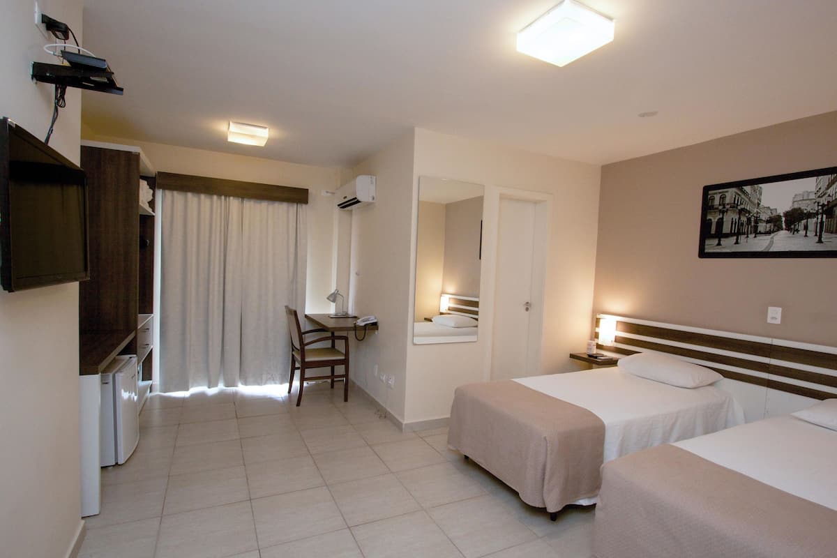Hotelkamer met twee bedden, een bureau met stoel, een kleine kitchenette en een badkamer zichtbaar door een geopende deur.