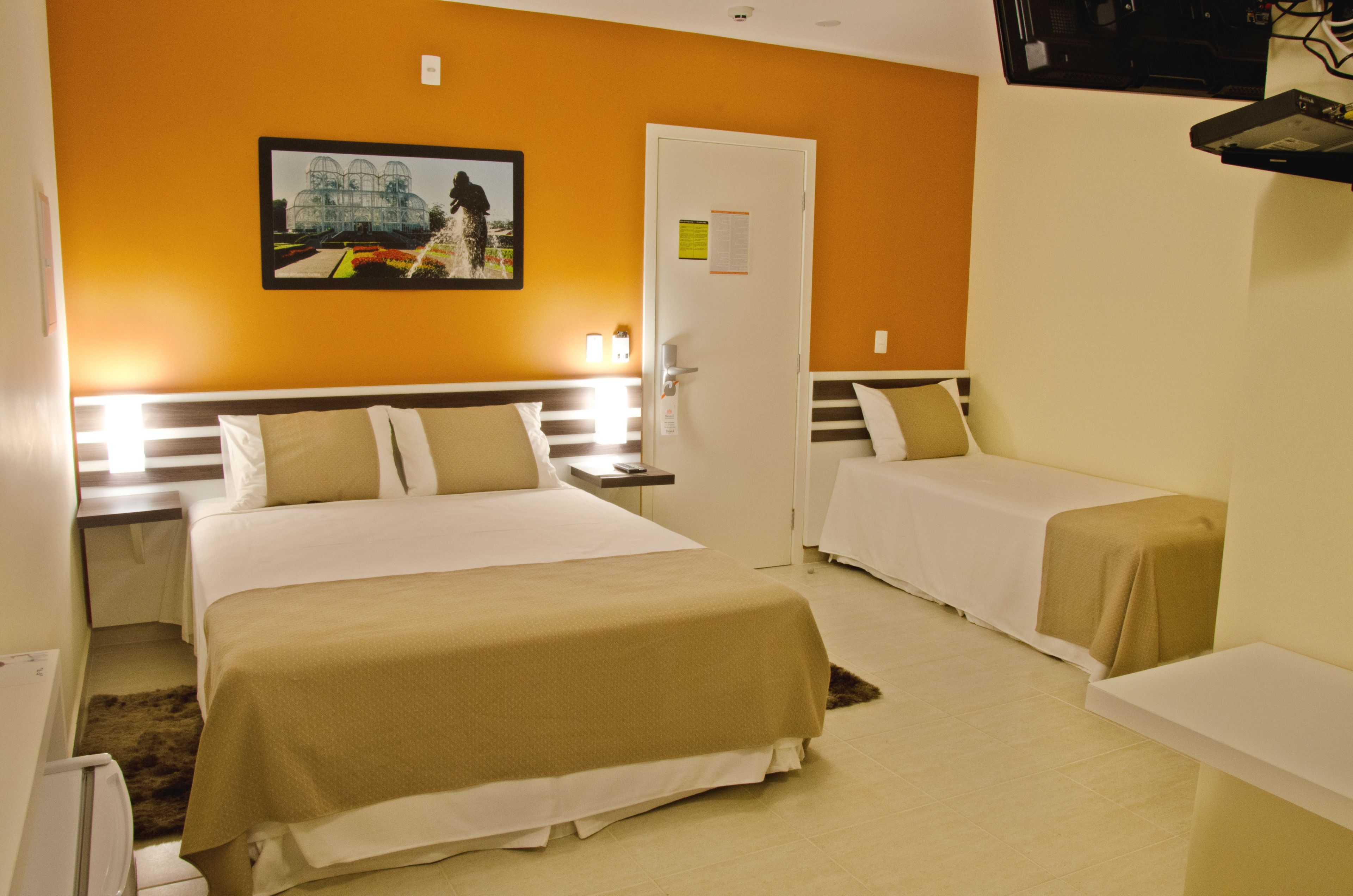 A hotel room with two beds, a door, a nightstand, and a wall-mounted TV.