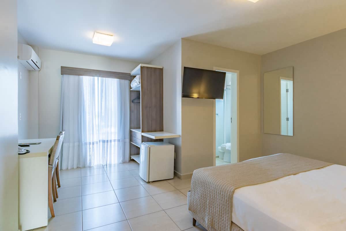 Een hotelkamer met een bed, een bureau, een koelkast, een kledingkast en een spiegel.