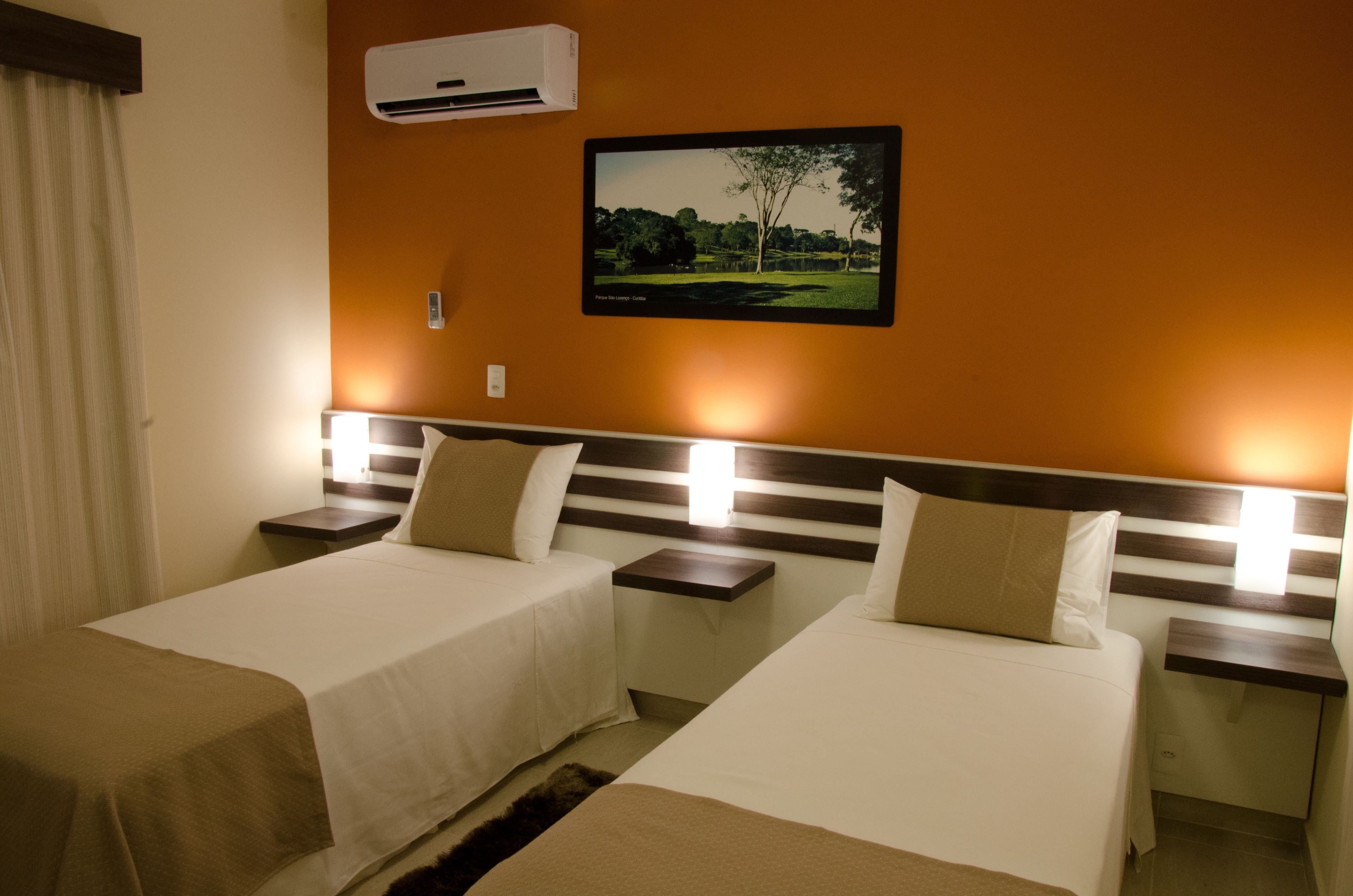 A hotel room with two beds, a flat-screen TV on the wall, and an air conditioning unit.