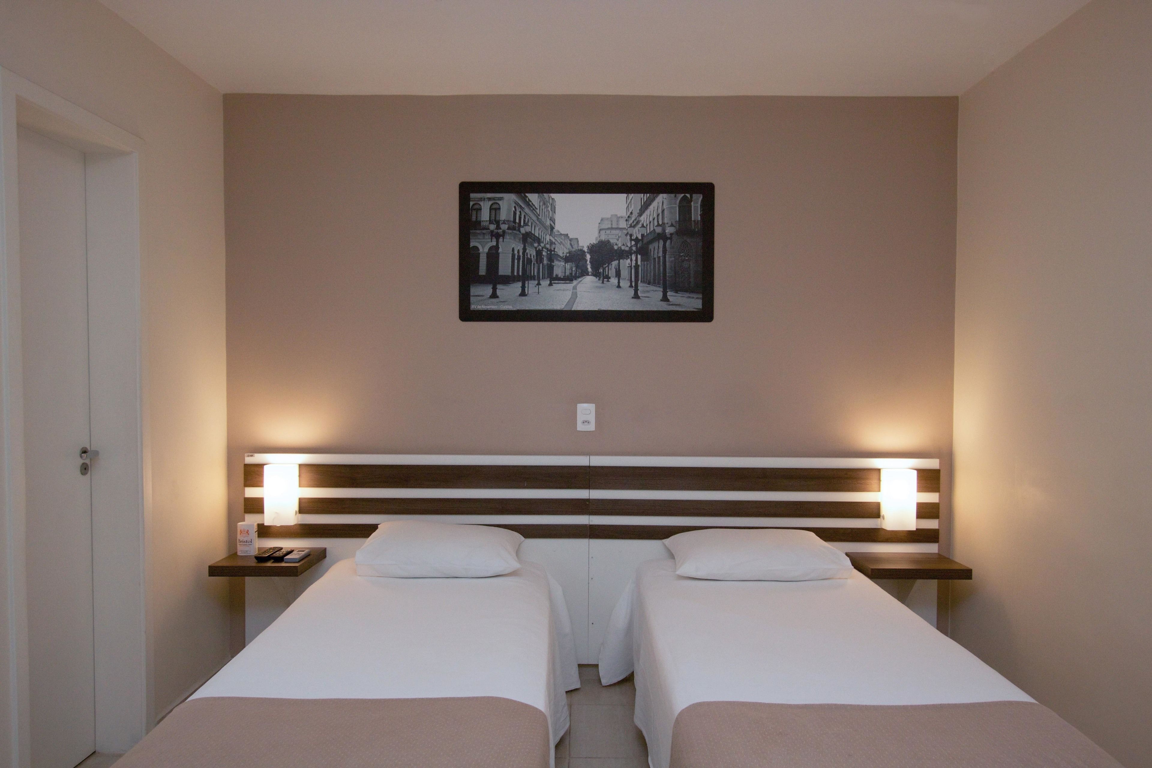 A hotel room with two beds, a nightstand, a wall-mounted picture, and a door.