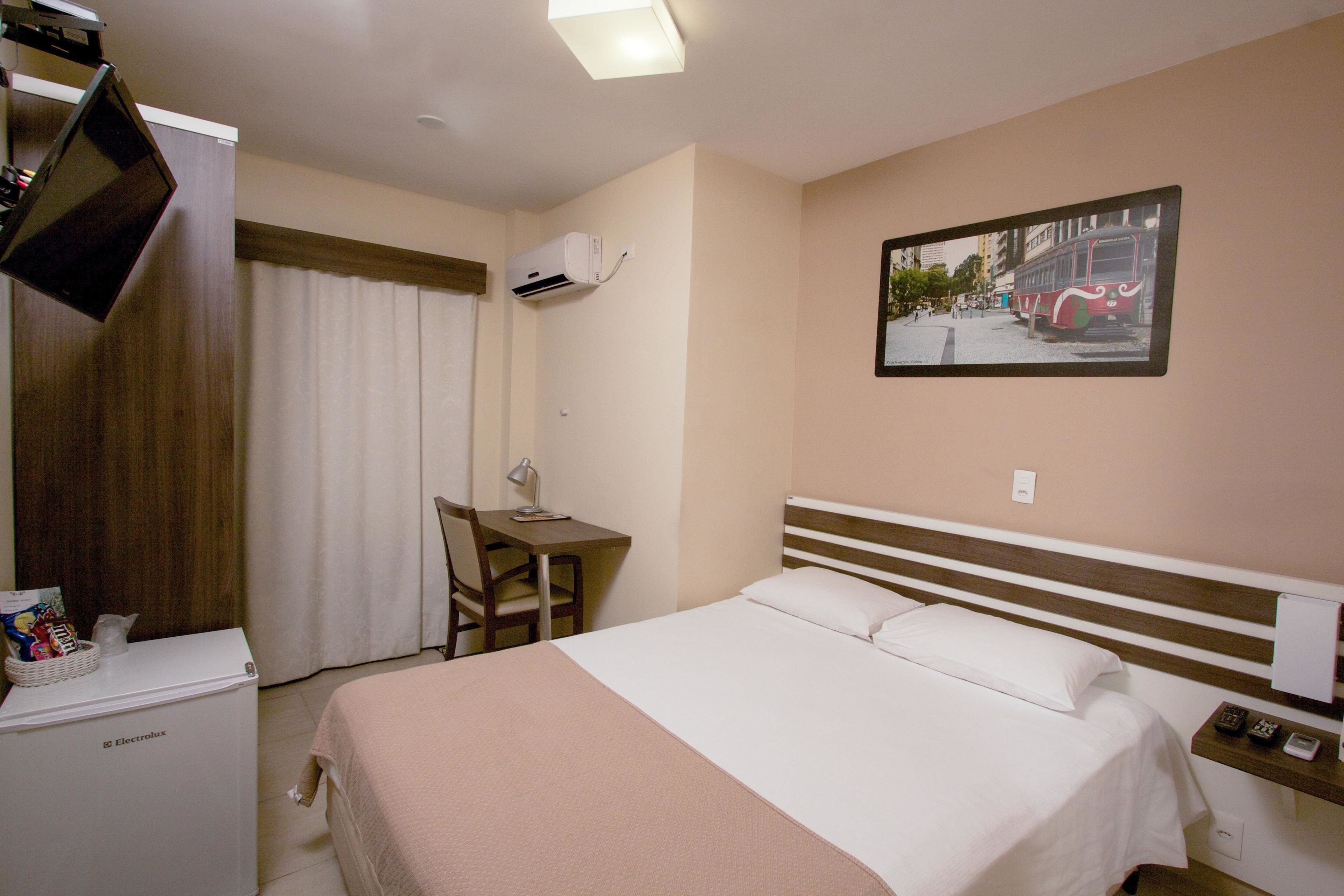 Ein Hotelzimmer mit einem Bett, einem Schreibtisch, einem Sessel, einem Fernseher und einer Wandklimaanlage.
