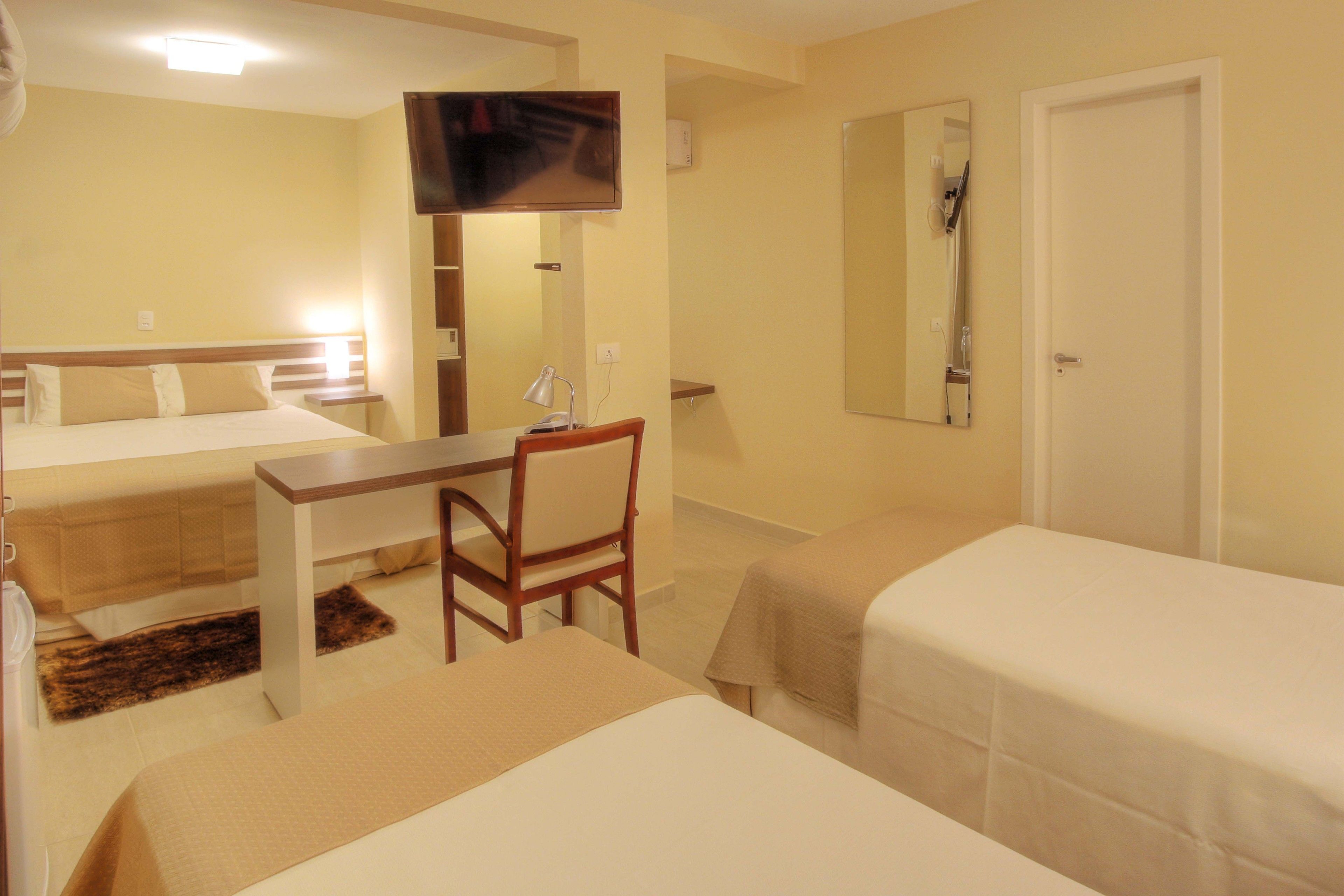 Habitación de hotel con dos camas, un escritorio, una silla, un televisor y un espejo.