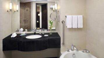 A modern bathroom with a black countertop sink, a large mirror, a bathtub, and a handrail.
