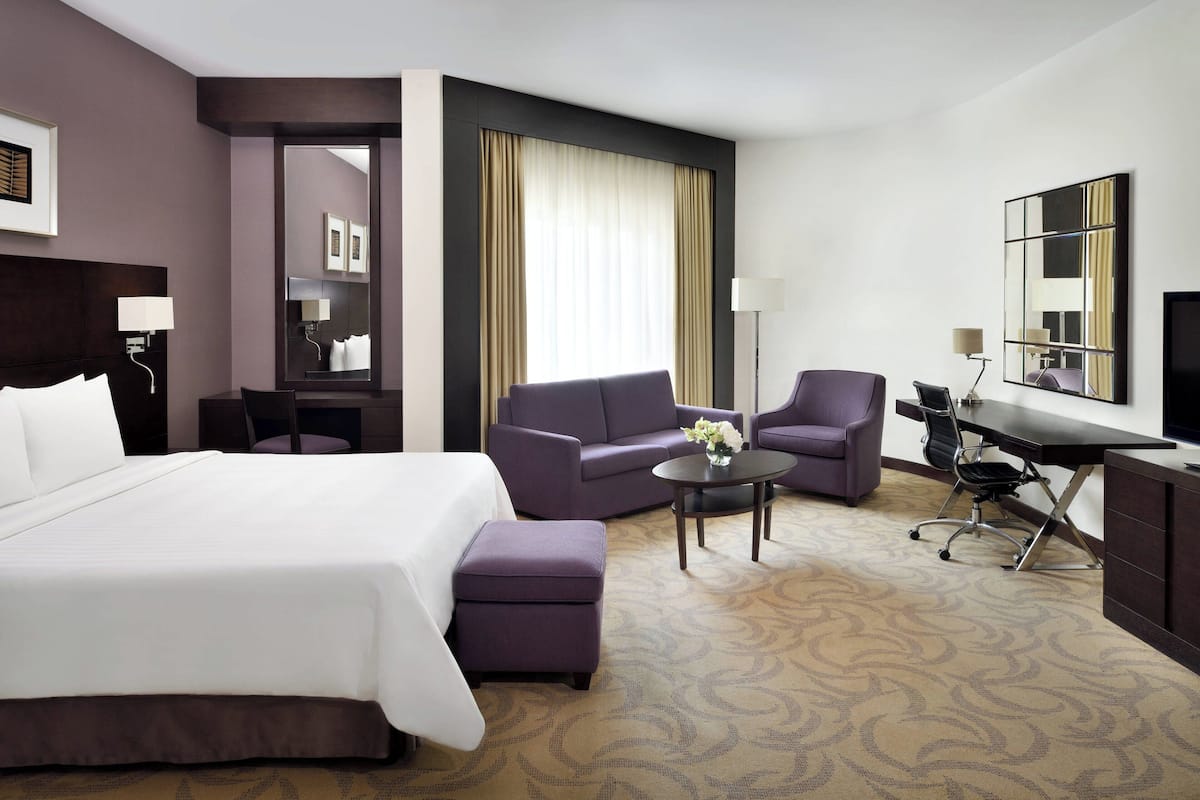 A hotel room with a large bed, a sofa, a desk, and a chair.