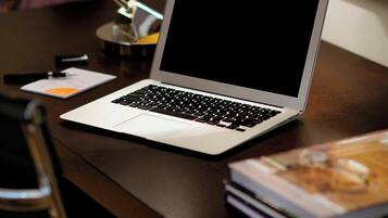 A laptop on a wooden desk with a lamp and a magazine.