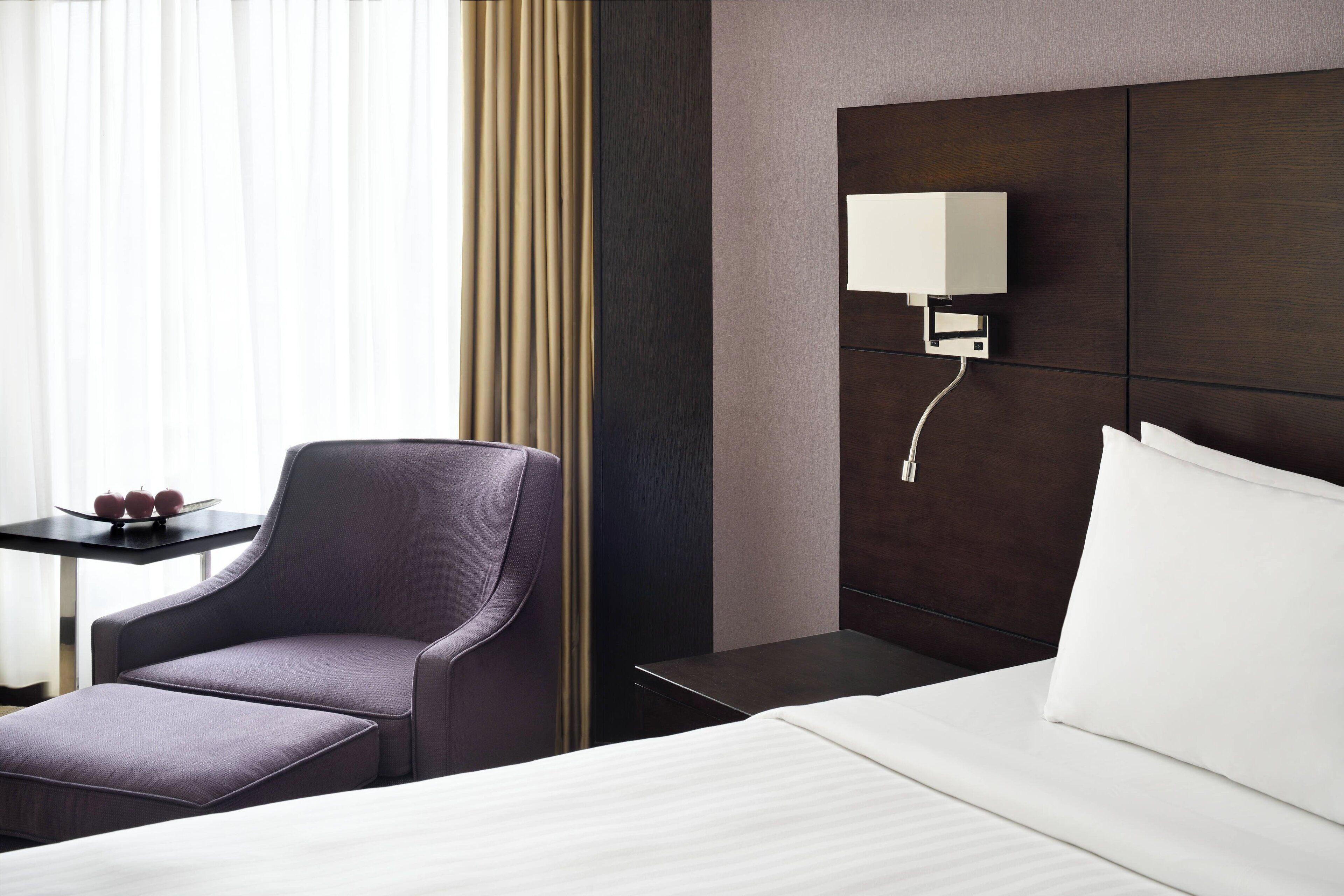 Ein Hotelzimmer mit Bett, Sessel, Nachttisch und einer Wandlampe.