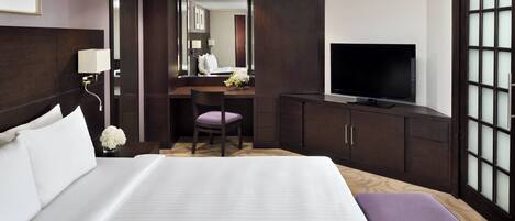 A hotel room with a large bed, a desk with a chair, a television, and a wardrobe.