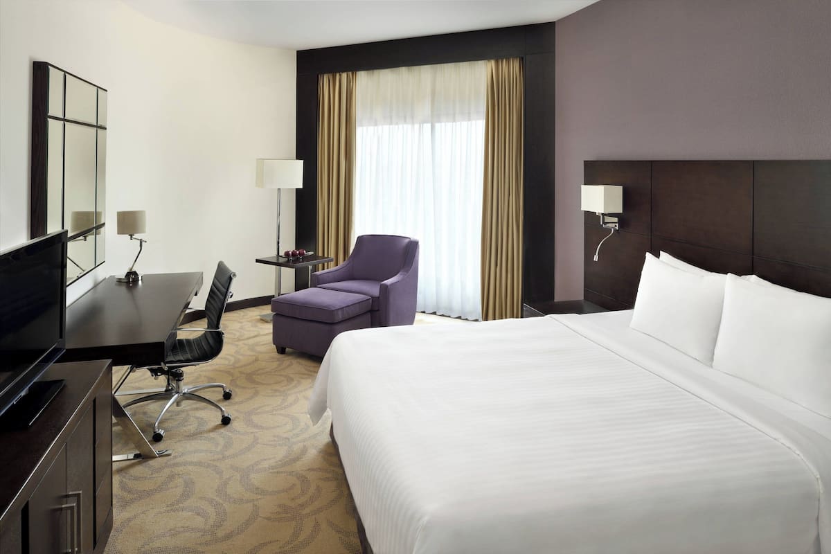 A hotel room with a large bed, a desk with a chair, a television, and a window with curtains.
