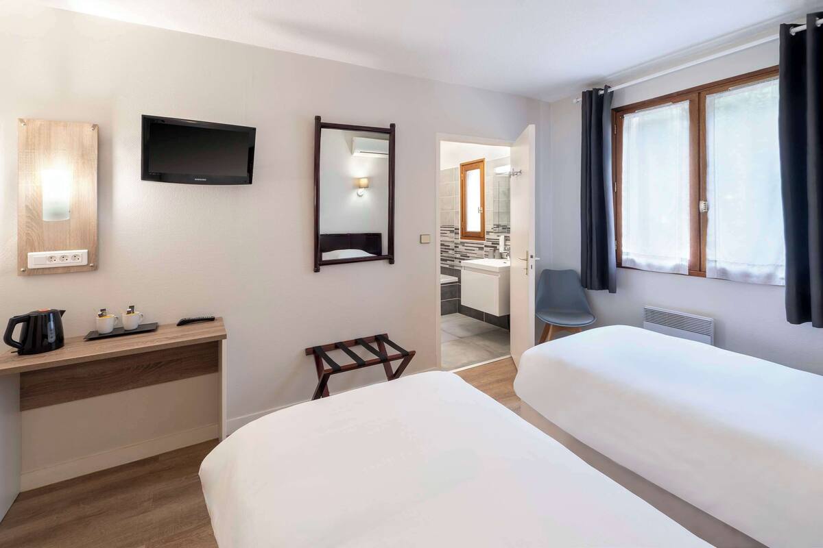 Une chambre d’hôtel avec un lit, un bureau doté d’un téléviseur à écran plat, un miroir et une salle de bain visible à travers une porte ouverte.