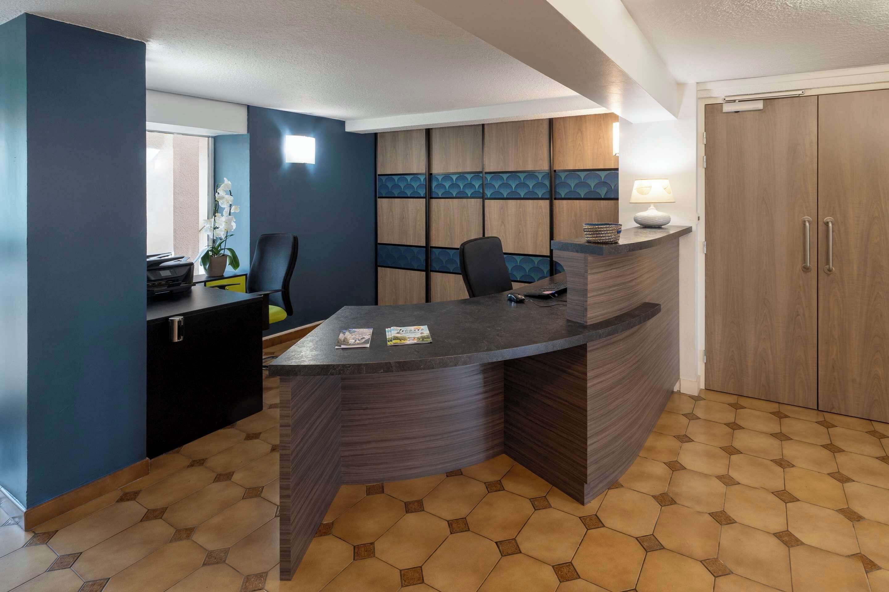 Un espace d’accueil moderne avec un comptoir incurvé, un coin salon et une grande armoire en bois.