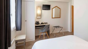 Ein Hotelzimmer mit Bett, Schreibtisch mit Stuhl, Fernseher, Spiegel und Wäscheständer.