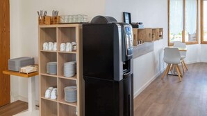 Eine moderne Küche mit einem schwarzen Kühlschrank, Holzregalen mit Tellern und einem Essbereich mit einem weißen Stuhl.