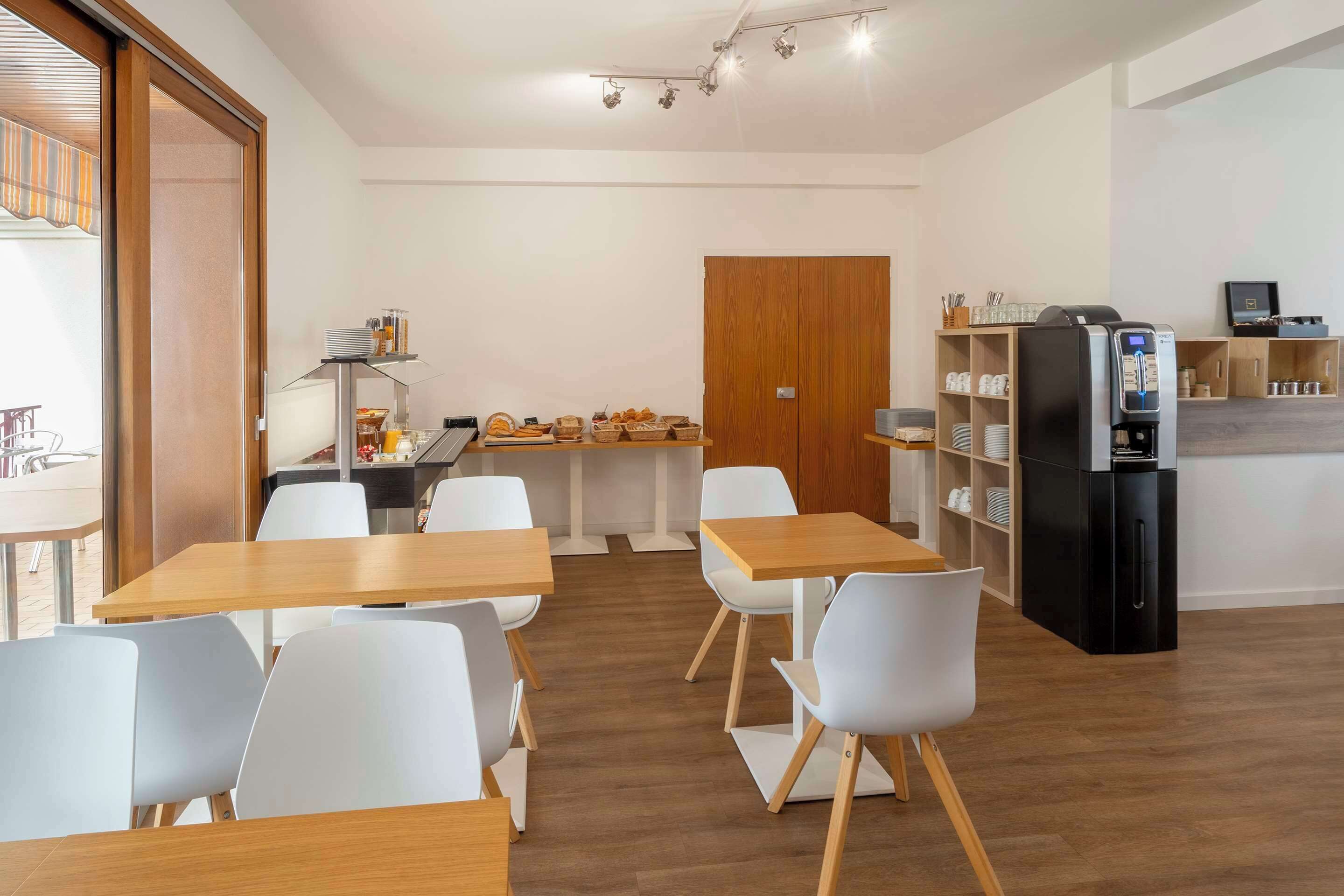A modern dining area with wooden tables and white chairs, a refrigerator, and a buffet with various food items.
