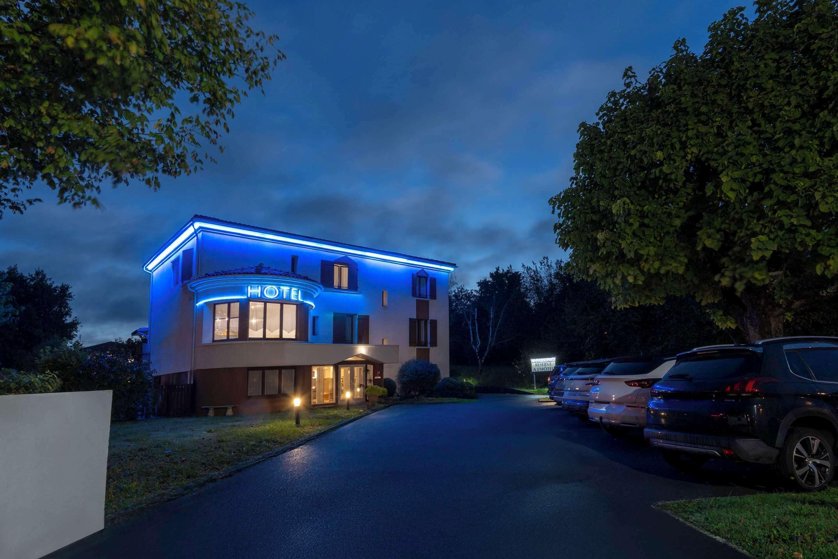 Un hotel de diseño moderno, con una entrada bien iluminada y un estacionamiento con varios coches.