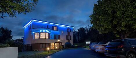 Un hotel de diseño moderno, con una entrada bien iluminada y un estacionamiento con varios coches.