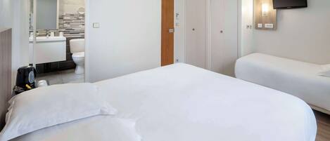 Habitación de hotel con una cama grande, una mesita de noche, un televisor montado en la pared y una zona de estar independiente con un sofá.