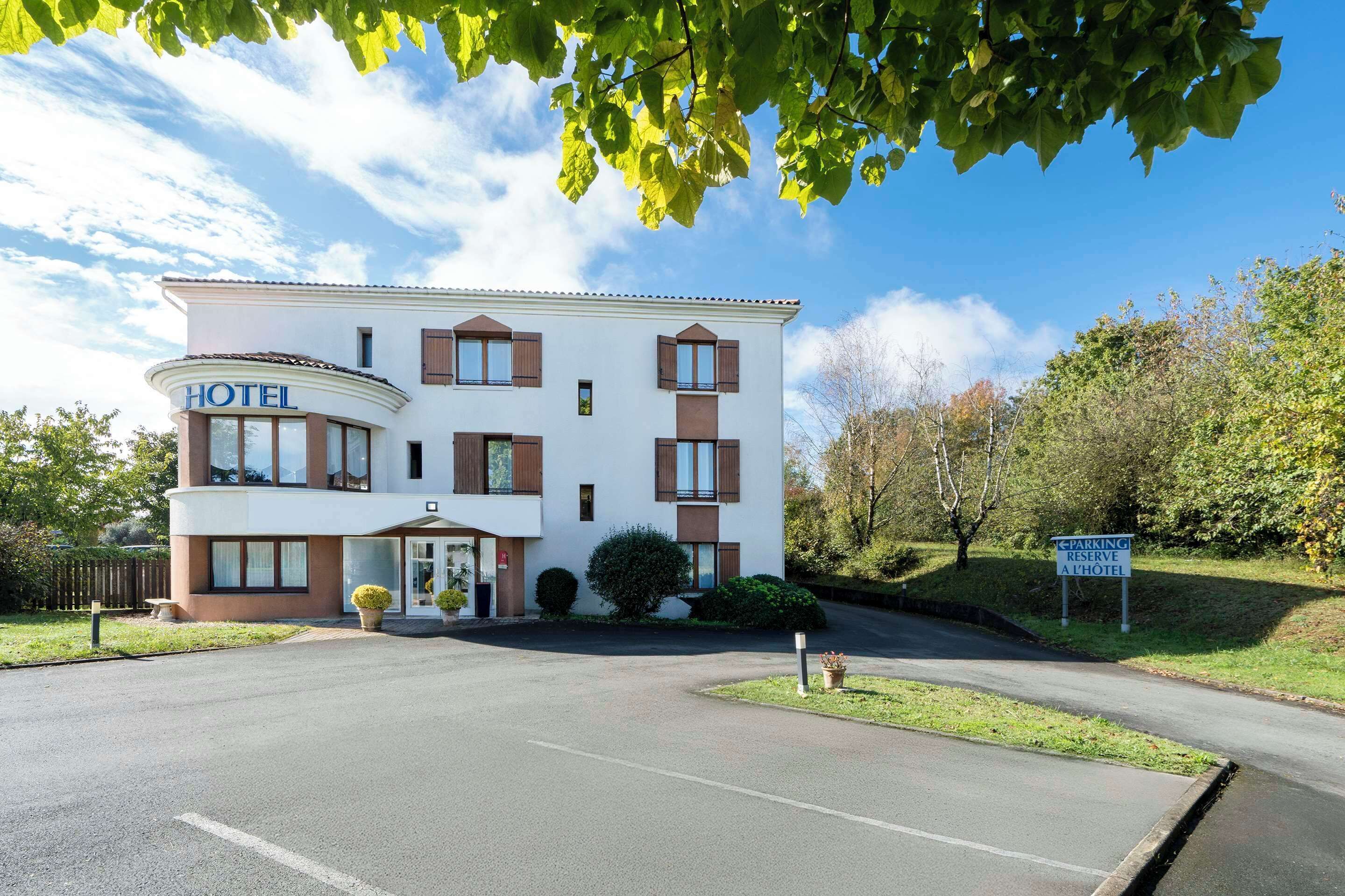 Un hotel con fachada blanca, contraventanas marrones y un letrero que indica una zona de estacionamiento reservada.