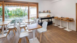 Ein moderner Essbereich mit weißen Stühlen und Tischen, eine Buffettheke mit Speisen und Blick auf Grünflächen.
