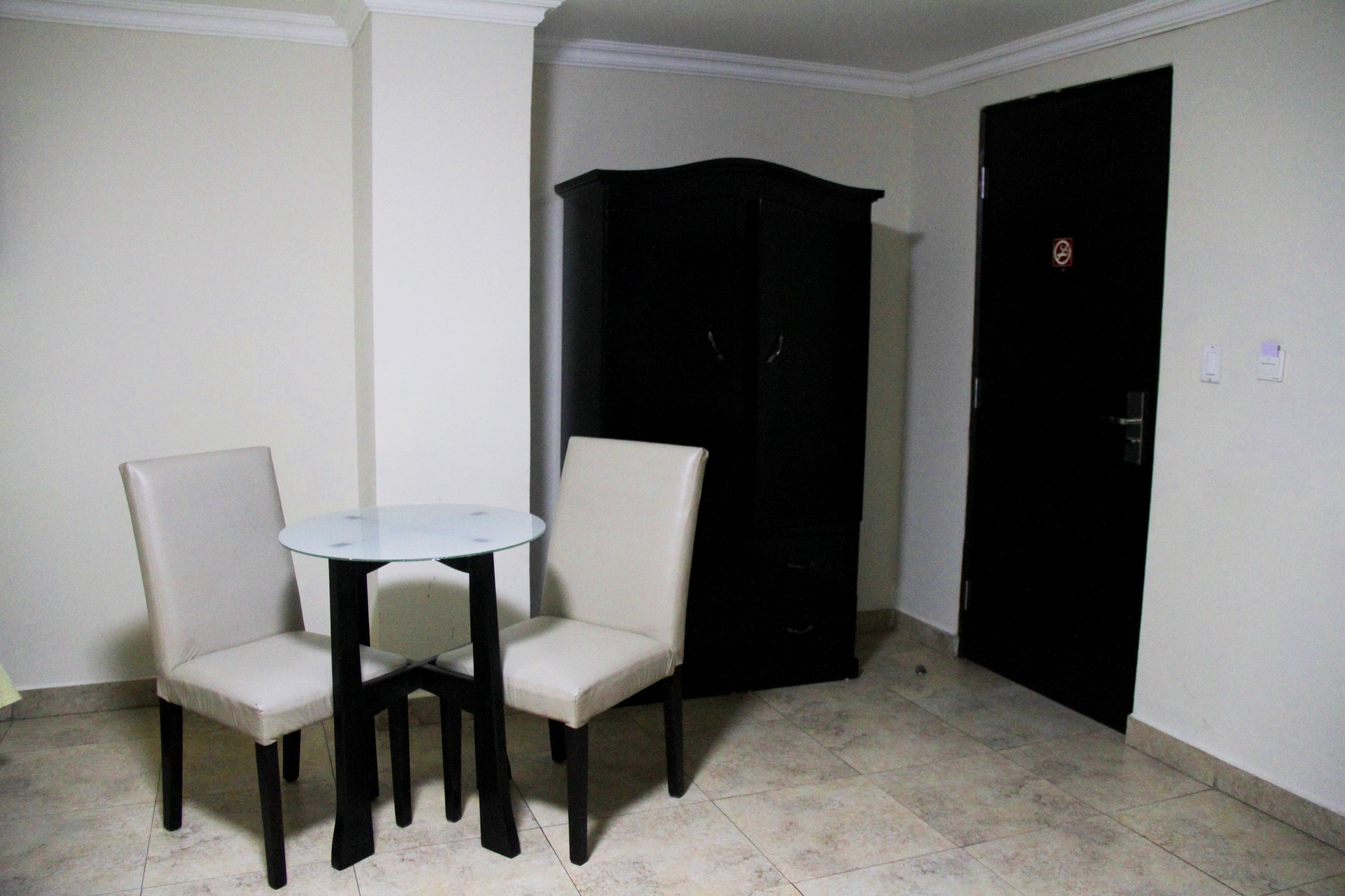 Een kamer met een kleine ronde tafel en twee stoelen, een zwarte garderobe en een gesloten deur met een verboden toegangsbord.