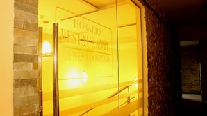 Una puerta de vidrio con el texto "HORARIO RESTAURANTE LUNES A DOMINGO" que indica los horarios de atención del restaurante.