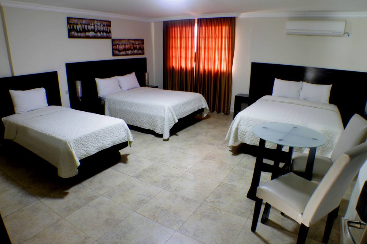 A hotel room with two beds, a small round table with a chair, and a window with curtains.