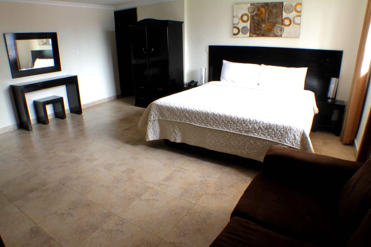 A hotel room with a large bed, a wardrobe, a vanity with a mirror, and a small table.