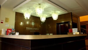Mostrador de recepción de hotel con candelabros, una mesa de registro y un cartel del Hotel Terranova.