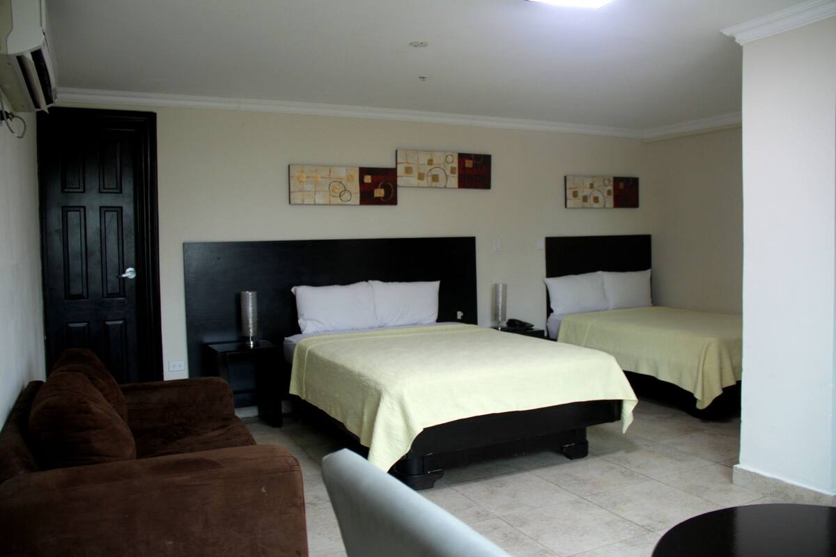 A hotel room with two beds, a sofa, a bedside table, and artwork on the walls.