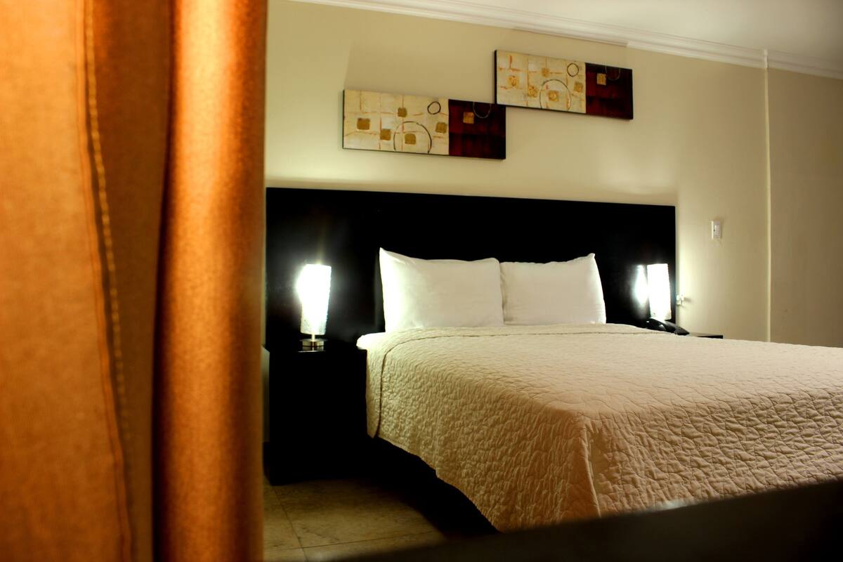A hotel room with a large bed, two bedside lamps, and abstract wall art.