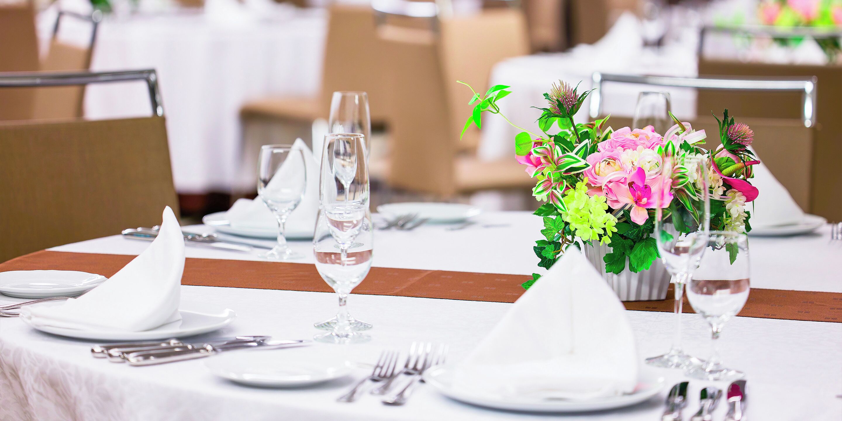 Una mesa dispuesta para un evento de cena formal, con manteles blancos, copas de cristal transparente y un centro de mesa floral.