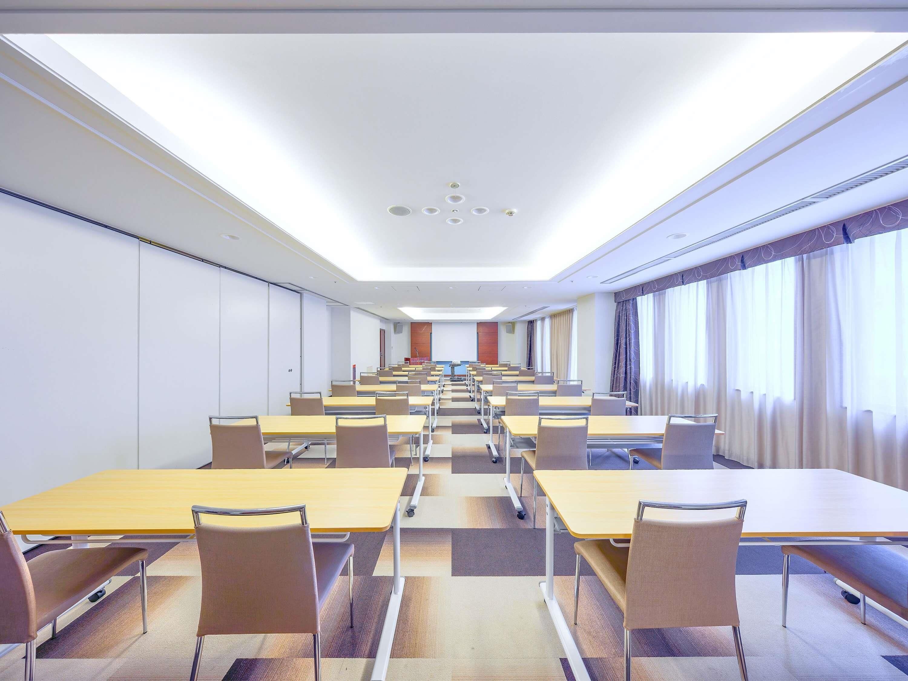 Un salón de conferencias con varias mesas y sillas, un techo con iluminación empotrada y ventanas amplias con cortinas.
