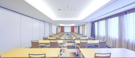 Un salón de conferencias con varias mesas y sillas, un techo con iluminación empotrada y ventanas amplias con cortinas.