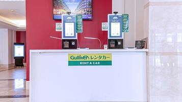 A rental car counter with a digital display, a sign for Gulliver Rent a Car, and a large screen in the background.