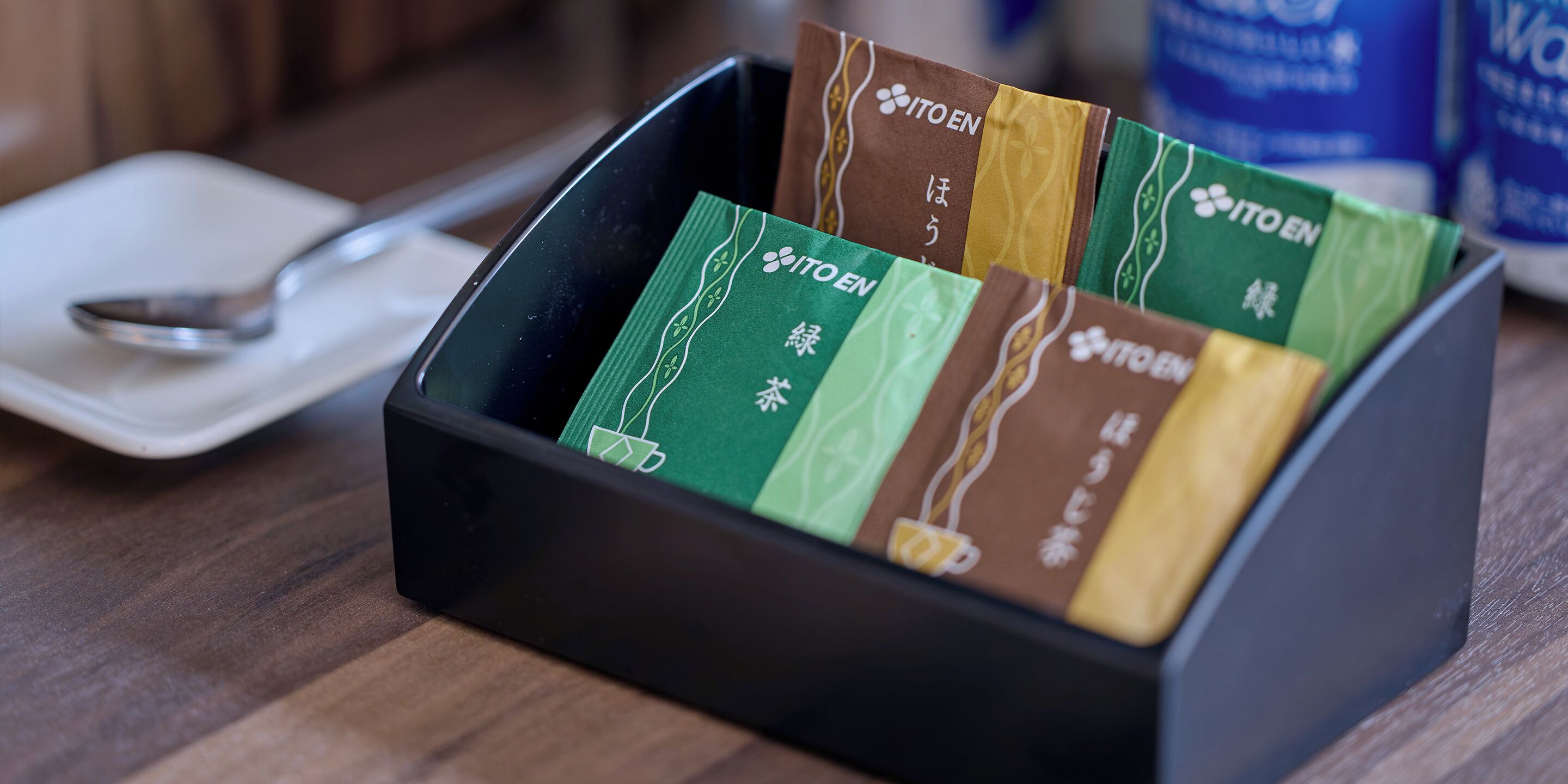 A black tray holding several ITO EN tea bags in green, brown, and yellow colors.