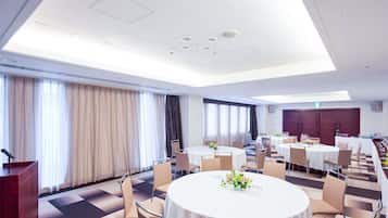 A conference room with round tables, chairs, a podium, and a large window with curtains.