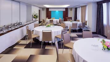 A hotel dining area with round tables, chairs, and buffet stations.