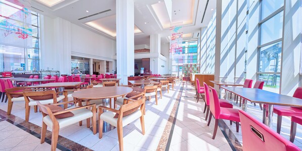 A spacious indoor dining area with multiple tables and chairs, large windows, and a modern architectural design.