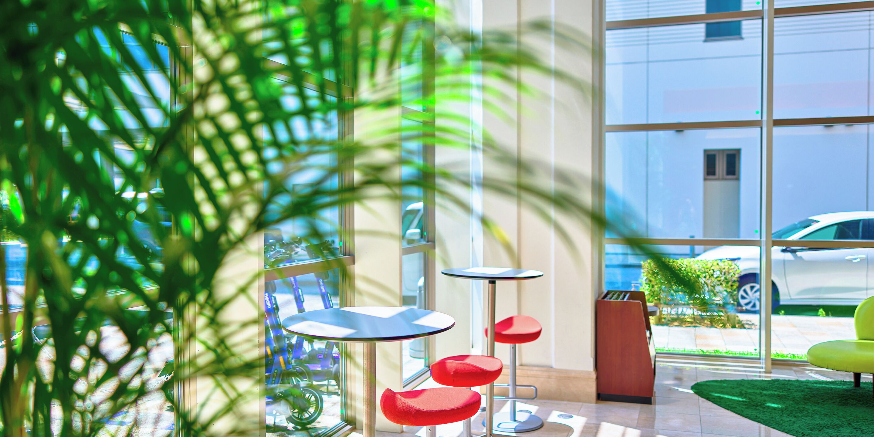 Un espace intérieur moderne doté de grandes fenêtres, d’une zone recouverte de gazon synthétique et d’un aménagement avec des chaises rouges et bleues.