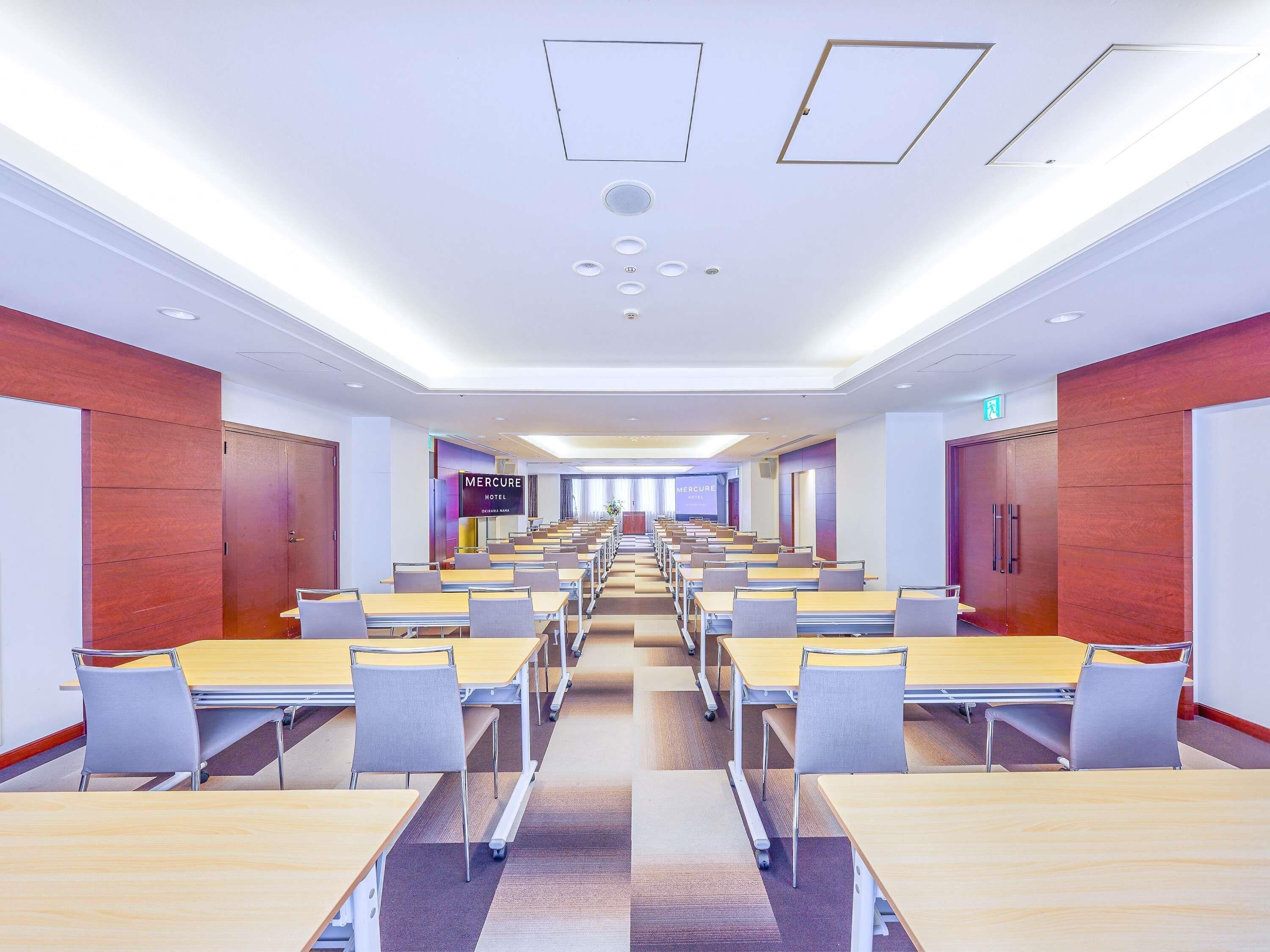 A conference room with rows of tables and chairs, wooden panel walls, and a sign for 'Mercure Hotel'.