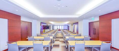 A conference room with rows of tables and chairs, wooden panel walls, and a sign for 'Mercure Hotel'.