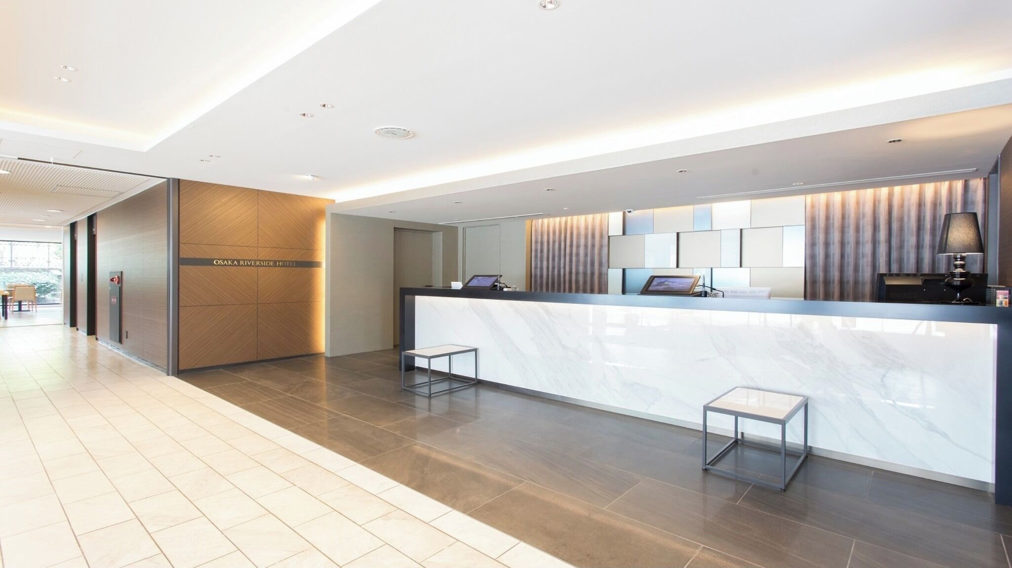 A hotel reception area with a marble counter, a digital screen, and a seating area.