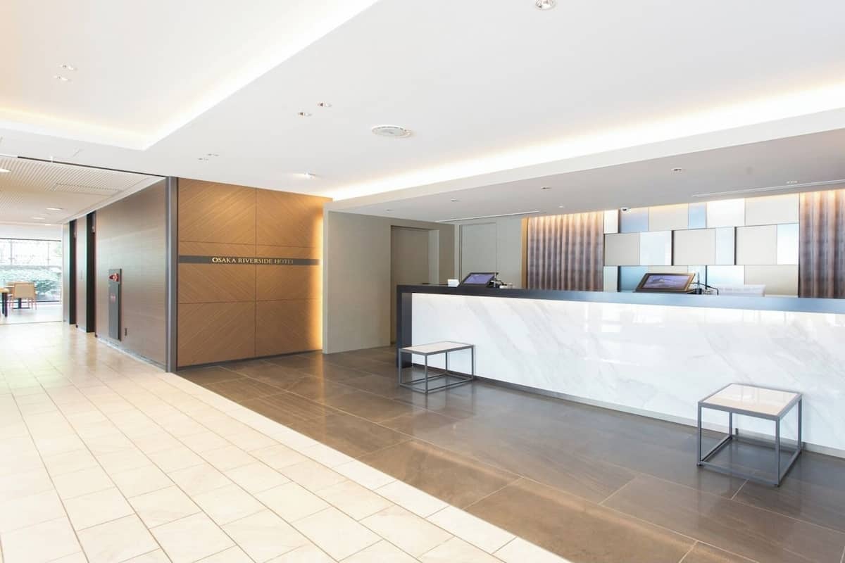 A hotel reception area with a marble counter, a digital screen, and a seating area.