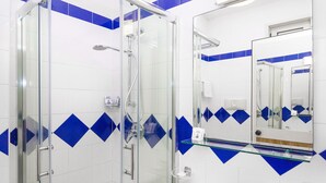 A modern bathroom with a glass-enclosed shower, white tiles with blue diamond patterns, a glass shelf, and a white sink with a towel.