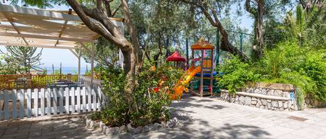 A covered outdoor area with a playground, stone wall, and trees.