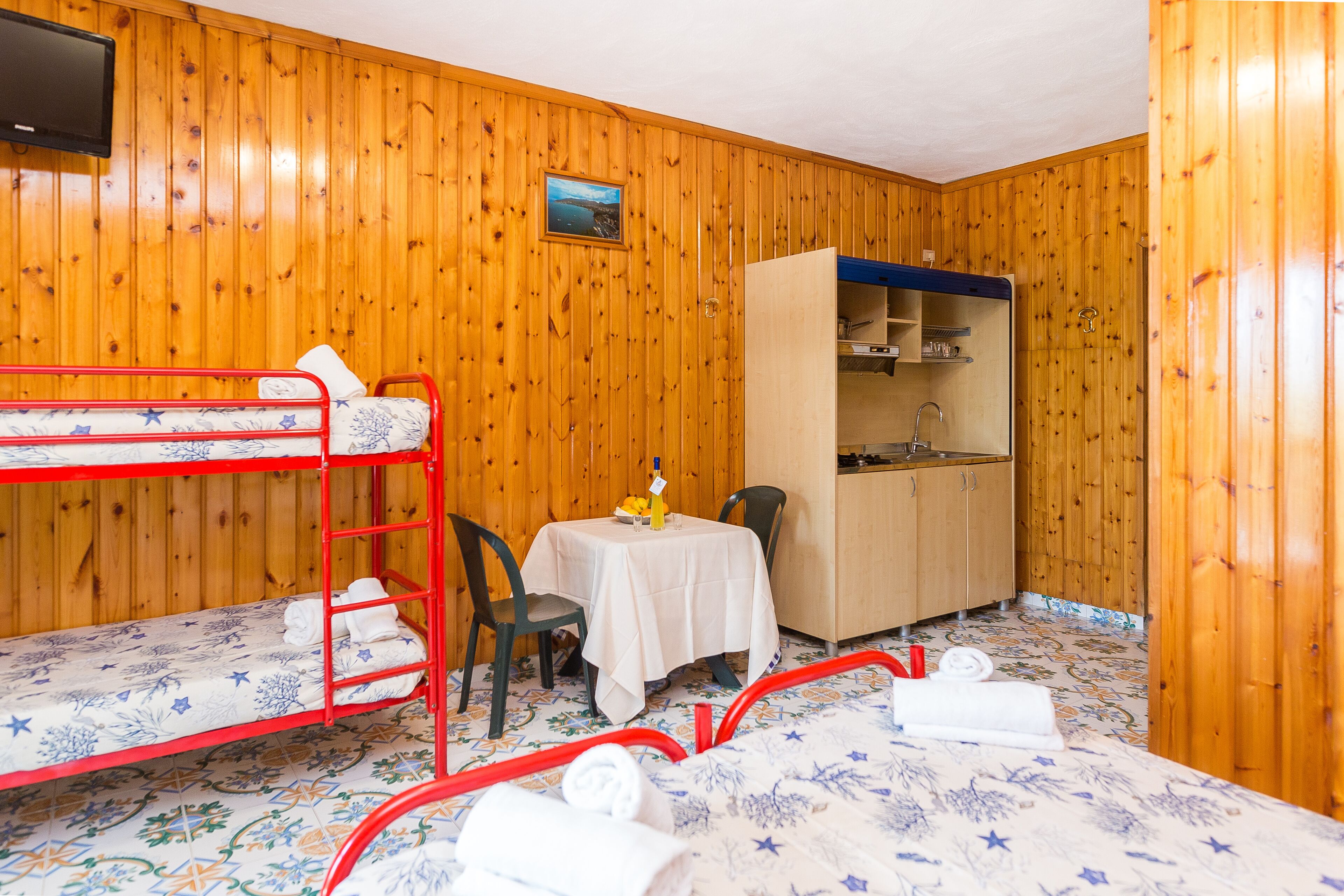 Une pièce aux murs en bois, avec des lits superposés, une petite table et une chaise, un placard et un téléviseur.