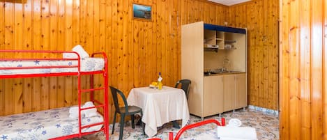 A room with wooden walls, bunk beds, a small table with a chair, a cabinet, and a television.