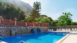 A swimming pool with a stone wall, a waterfall feature, and lounge chairs.